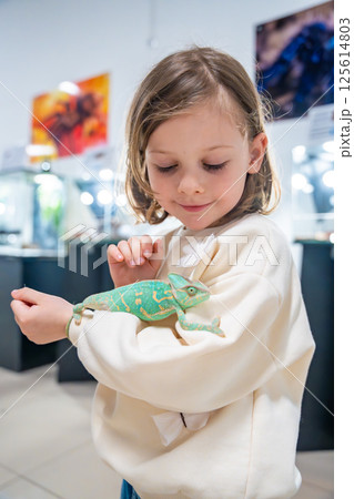 Little girl holding a green chameleon in her hands. Concept of childhood curiosity, interaction with exotic animals, and early interest in biology 125614803