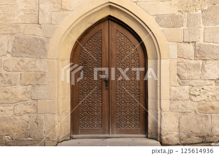 Beautiful handcrafted wooden door set within a detailed stone archway Beautiful handcrafted wooden door set within a detailed stone archway 125614936