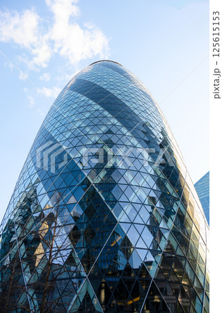 Captured against the blue sky, the Gherkin stands prominently in London's financial district, showcasing its distinctive design and glass facade with reflections of the city around it. Captured against the blue sky, the Gherkin stands prominently in London's financial district, showcasing its distinctive design and glass facade with reflections of the city around it. 125615153