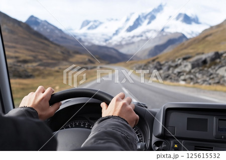 Driving towards majestic snowy mountain range POV, hands grip steering wheel on winding road, epic mountain landscape unfolds ahead, perfect for adventure travel mountain themed content. 125615532
