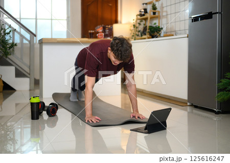 Active man doing plank exercise on mat and following an online workout on digital tablet Active man doing plank exercise on mat and following an online workout on digital tablet 125616247