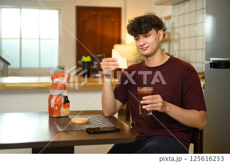 Young caucasian man enjoying a protein shake and sandwich at the kitchen table Young caucasian man enjoying a protein shake and sandwich at the kitchen table 125616253