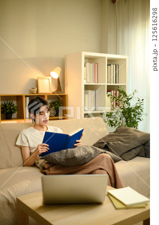 Young man reading a book while relaxing on sofa in a bright living room Young man reading a book while relaxing on sofa in a bright living room 125616298