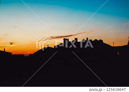 The castle on the mountain against the sunset sky. Abstract village, town in sunrise. Houses and towers on a hill at dusk, in twilight. Sunlight sky. 125616647