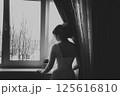 A girl in a wedding dress stands at the window with her back to the viewer. Black and white photo 125616810