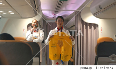 Asian stewardess safety explaining passengers prior to flight take off in airplane, air hostess uniform safety demonstration presenting pre-flight safety instructions life vest in emergency situation Asian stewardess safety explaining passengers prior to flight take off in airplane, air hostess uniform safety demonstration presenting pre-flight safety instructions life vest in emergency situation 125617673