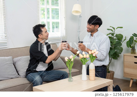 LGBT Friendship and Coffee. Two men enjoying a warm moment with coffee, celebrating their friendship in a cozy living room. 125617979