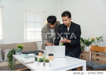 Team Collaboration and Project Review. Two professionals working together on a laptop in a modern office setting. Team Collaboration and Project Review. Two professionals working together on a laptop in a modern office setting. 125617985