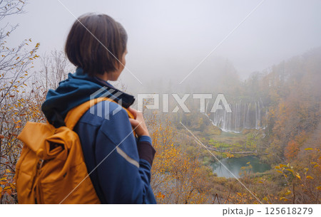 Plitvice Lakes in Croatia during autumn, showcasing stunning waterfalls, vibrant foliage. Woman is viewing on national park from above, viewpoint in forest under lakes 125618279