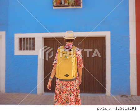 Woman in dress strolls through colorful streets of Spanish coastal town of La Vila Joiosa . sunny winter atmosphere highlights charm of Mediterranean architecture and quiet seaside life, back view Woman in dress strolls through colorful streets of Spanish coastal town of La Vila Joiosa . sunny winter atmosphere highlights charm of Mediterranean architecture and quiet seaside life, back view 125618291