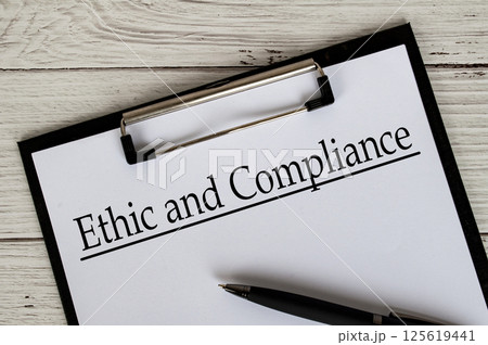 Clipboard with a document titled Ethic and Compliance text, placed on a white wooden surface. Clipboard with a document titled Ethic and Compliance text, placed on a white wooden surface. 125619441