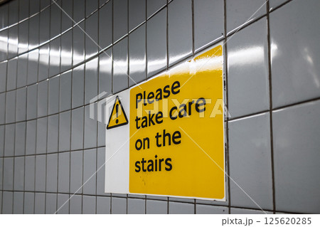 Caution sign on tiled wall warning pedestrians to take care on the stairs indoors Caution sign on tiled wall warning pedestrians to take care on the stairs indoors 125620285
