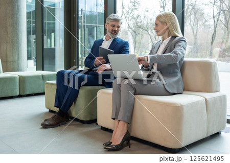 Businessman and woman manager sitting on sofa in office discussing corporate ideas 125621495