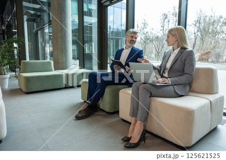 Manager and colleague using laptop on couch analyzing business plan in office Manager and colleague using laptop on couch analyzing business plan in office 125621525