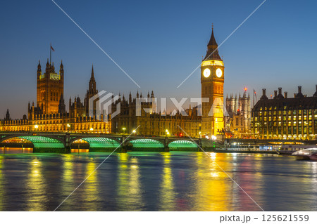 Illuminated Houses of Parliament and Big Ben reflect in the river as Westminster Bridge shines under the evening sky in London, creating a stunning night view of this historic landmark. 125621559