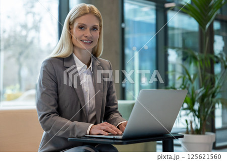 Smiling attractive employee using laptop on couch for online work Smiling attractive employee using laptop on couch for online work 125621560