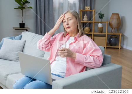 Mid aged woman in pink shirt feeling unwell and having a headache Mid aged woman in pink shirt feeling unwell and having a headache 125622105