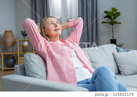 Smiling mid aged woman in pink shirt looking contented while spending time at home Smiling mid aged woman in pink shirt looking contented while spending time at home 125622179
