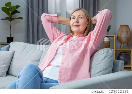 Smiling mid aged woman in pink shirt looking contented while spending time at home 125622181