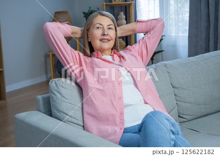 Smiling mid aged woman in pink shirt looking contented while spending time at home 125622182
