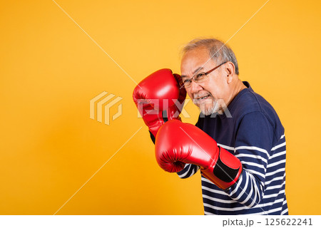 Portrait Asian old man wearing glasses wear two red boxing gloves studio shot isolated yellow background, smiling happy elderly man gray haired healthy fighter lifestyle concept 125622241