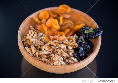 Prunes, dried apricots and nuts in a wooden bowl on a dark background 125622597