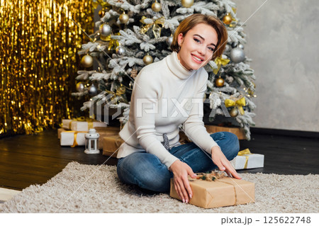 Woman smiling and decorating Christmas tree with new year gifts with toys Woman smiling and decorating Christmas tree with new year gifts with toys 125622748