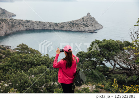 Woman taking pictures of landscape from mountaintop on a hike Woman taking pictures of landscape from mountaintop on a hike 125622893