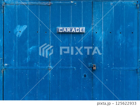 Blue wooden garage door with the inscription - Garage. Closed garage gate with a small lock on it 125622933