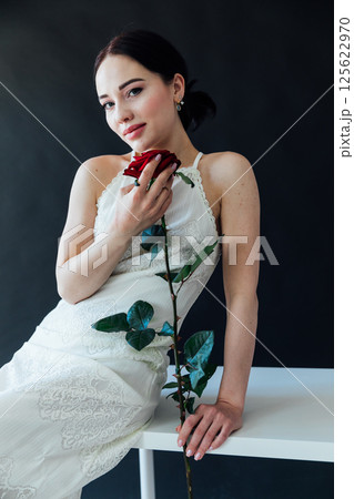 woman in white wedding dress sitting with red rose and smiling 125622970