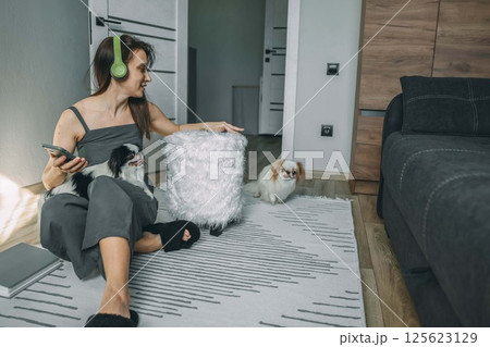 woman in casual wear with headphones interacting with her dogs in a modern living space, capturing a moment of joyful pet companionship 125623129
