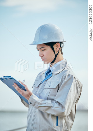 メモを取る作業着姿の20代の若い男性 メモを取る作業着姿の20代の若い男性 125623309