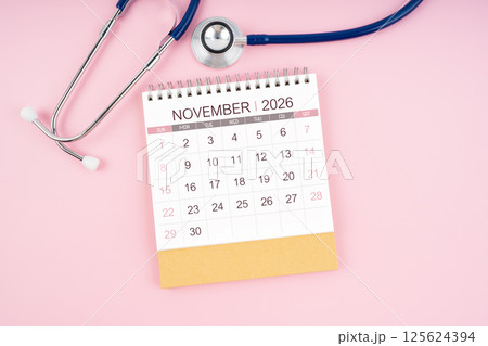 November 2026 desk calendar and Medical stethoscope on  pink background. 125624394