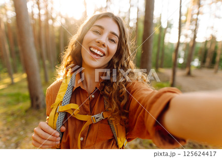 Beautiful woman taking picture of herself while walking in sunny forest. Selfie in nature. Adventure 125624417