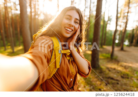 Beautiful woman taking picture of herself while walking in sunny forest. Selfie in nature. Adventure 125624418