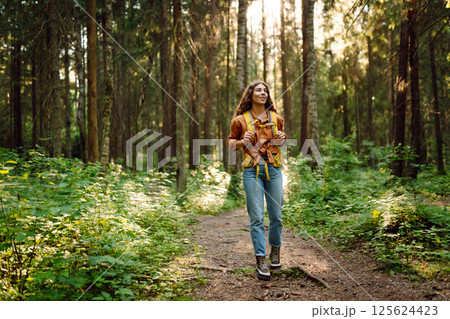 Tourist woman hiking alone in thick autumn forest. Stylish female looks for pathway among trees. Tourist woman hiking alone in thick autumn forest. Stylish female looks for pathway among trees. 125624423