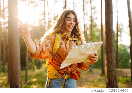 A traveler woman stands in a lush forest, examining a map with a focused expression 125624492