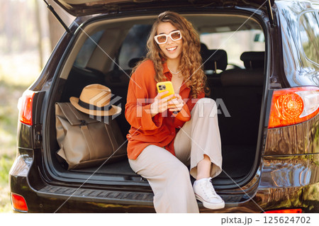 Beautiful woman sits in the trunk of a car outdoor and uses a smartphone. Lifestyle Beautiful woman sits in the trunk of a car outdoor and uses a smartphone. Lifestyle 125624702