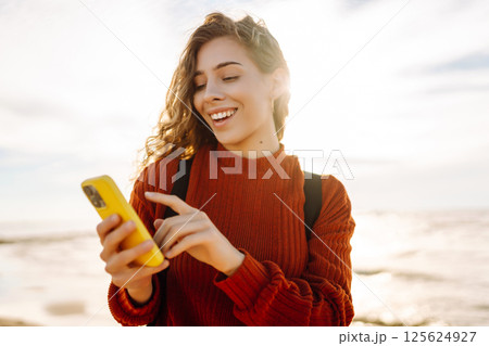 Young woman using mobile phone at beach. Cold weather. Autumn. Blogging, communication 125624927