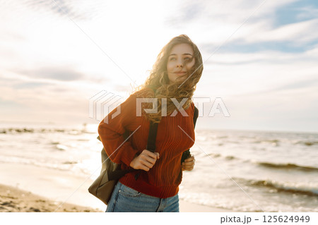 As she walked along the beach, the woman tourist adjusted her backpack, taking in the salty sea air 125624949