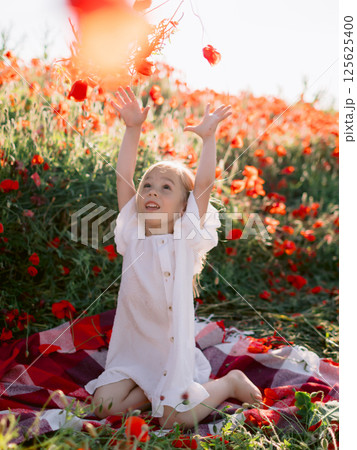 Little girl in dress on red plaid in a poppy field, throws flowers and enjoying a sunny summer day Little girl in dress on red plaid in a poppy field, throws flowers and enjoying a sunny summer day 125625400