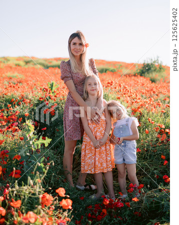 Mother with daughters posing in a blooming poppy field. Beauty woman and kids in dress with red flowers Mother with daughters posing in a blooming poppy field. Beauty woman and kids in dress with red flowers 125625402