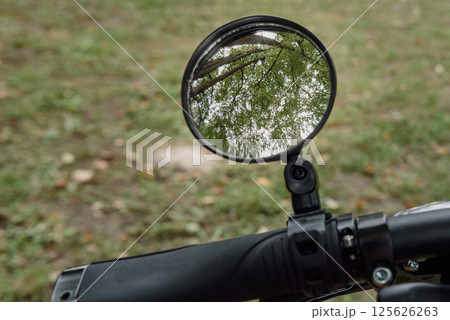 A close-up of a bicycle handlebar mirror reflecting lush green trees, symbolizing the freedom of outdoor adventure 125626263