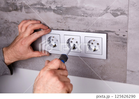 A man uses a screwdriver to install an electrical outlet on a porcelain tile wall 125626290