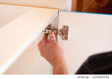 Installing a furniture hinge on the door. Assembling furniture and fixing fittings Installing a furniture hinge on the door. Assembling furniture and fixing fittings 125626291