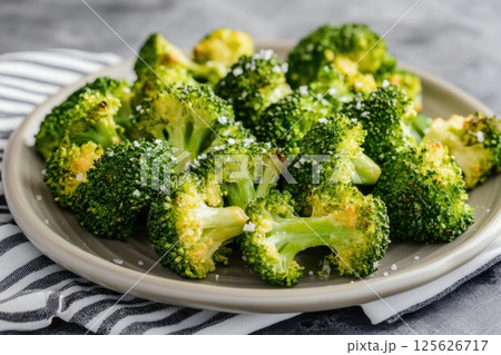 Close-up of roasted broccoli florets sprinkled with sea salt on a ceramic plate. Healthy vegan meal served on a striped napkin, ideal for clean eating and plant-based food concepts. Copy space 125626717