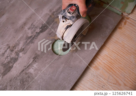 A construction worker uses an electric tool to cut a granite sheet on a wooden floor in a well-lit workshop 125626741