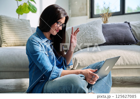 Young woman looking at laptop screen talking having video call sitting at home 125627085