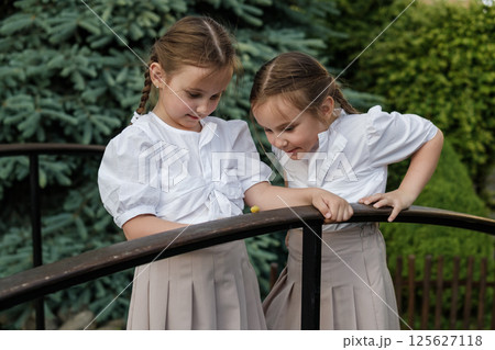 Little twins in light clothing lean over the snail. The girls stand near the railing, observing nature. 125627118