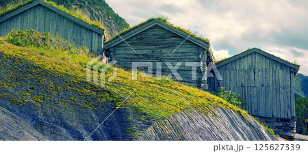 Old grunge wooden fishermen's house with green grass on roofs against fjord Old grunge wooden fishermen's house with green grass on roofs against fjord 125627339